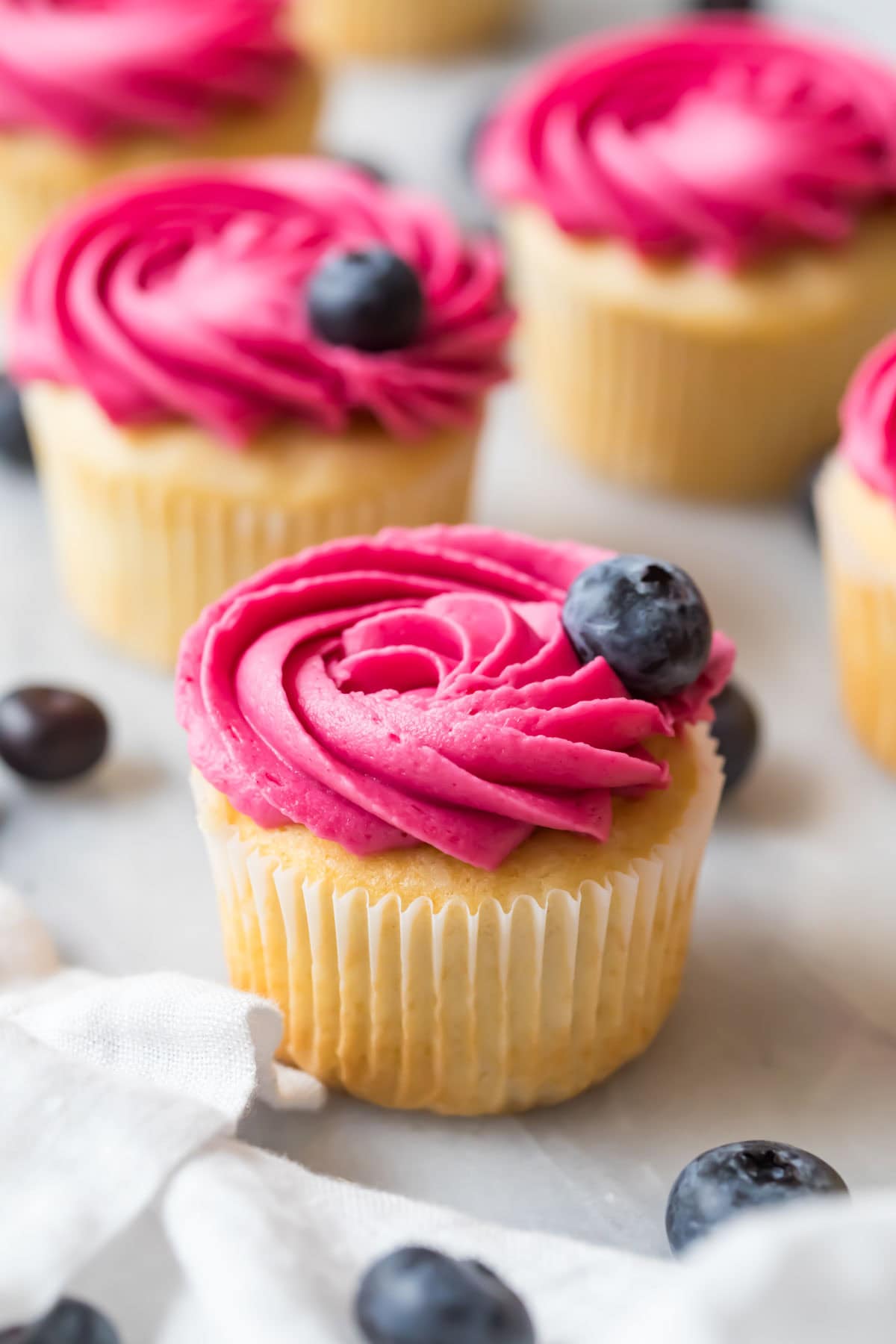 Cupcake frosted with a vibrantly colored blueberry frosting rosette and a blueberry garnish.