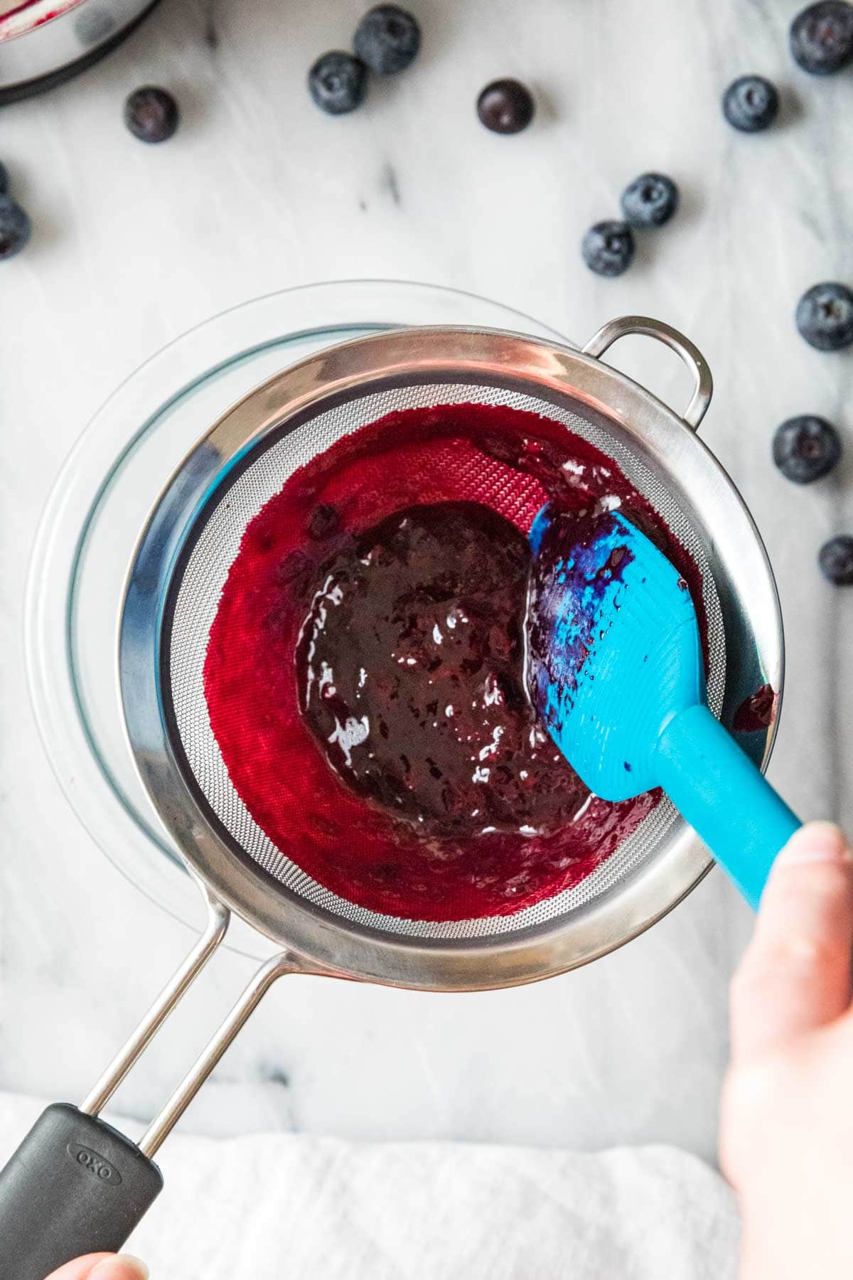 Blueberry sauce being strained through a fine mesh strainer.