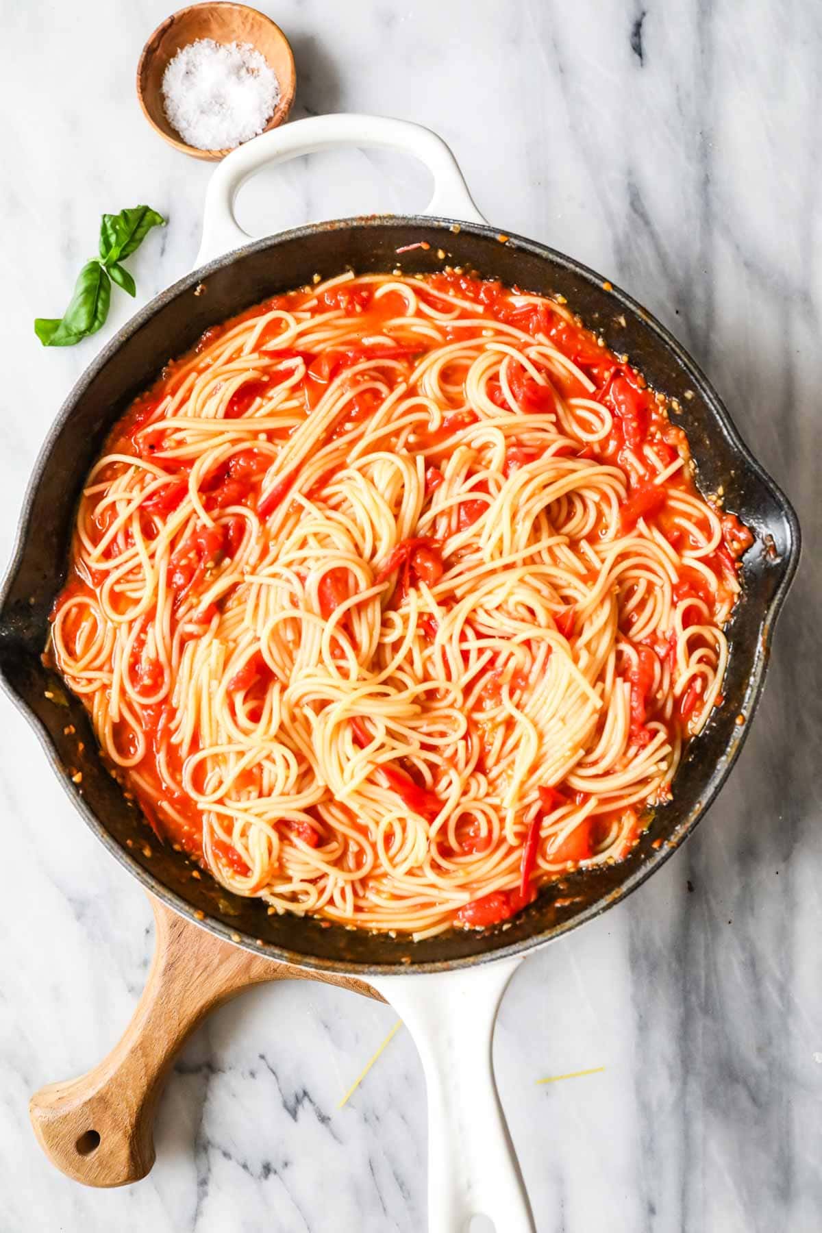 Overhead view of a skillet of spaghetti tossed with a sauce made from cherry tomatoes.