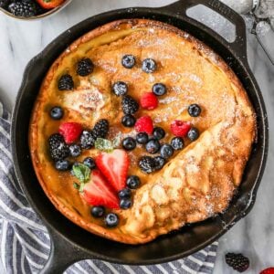 Overhead view of a Dutch baby topped with fresh berries and powdered sugar in a cast iron skillet.