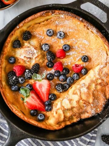 Overhead view of a Dutch baby topped with fresh berries and powdered sugar in a cast iron skillet.