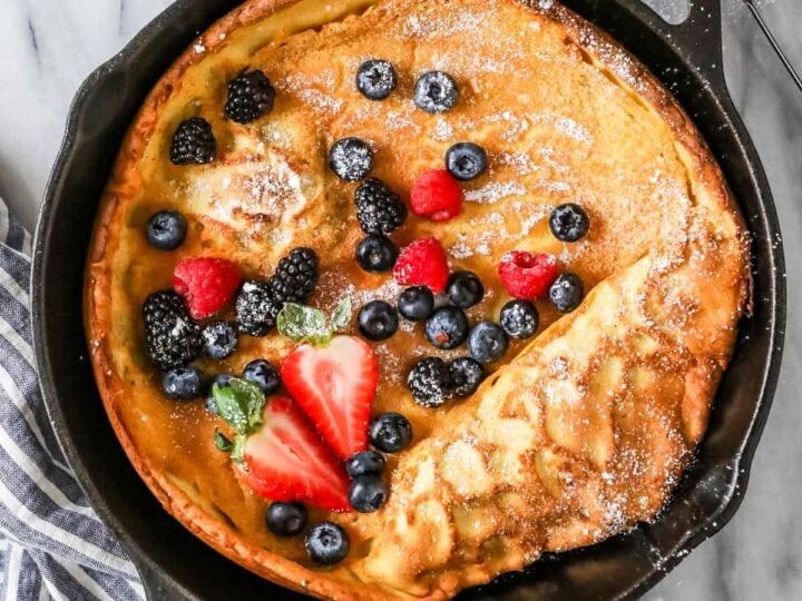 Overhead view of a Dutch baby topped with fresh berries and powdered sugar in a cast iron skillet.