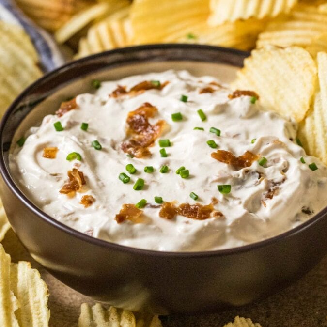 Bowl of homemade french onion dip surrounded by ripple chips.