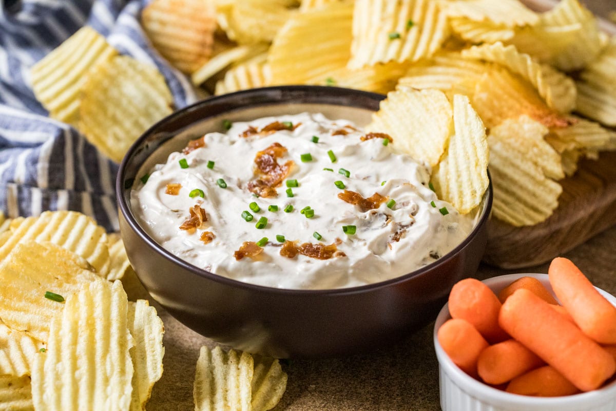 Bowl of homemade french onion dip surrounded by ripple chips.
