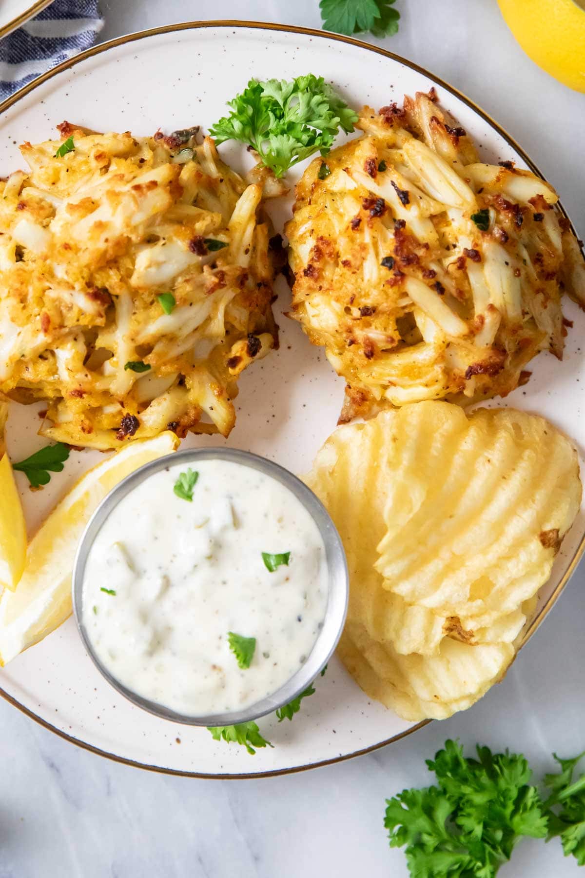 Overhead view of tartar sauce with crab cakes and potato chips.