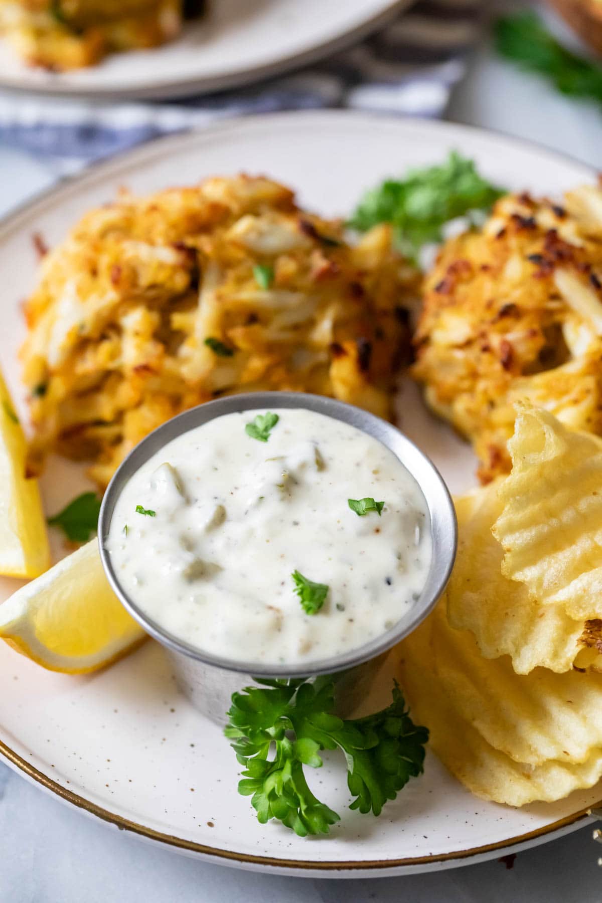 Dish of tartar sauce beside crab cakes and potato chips.