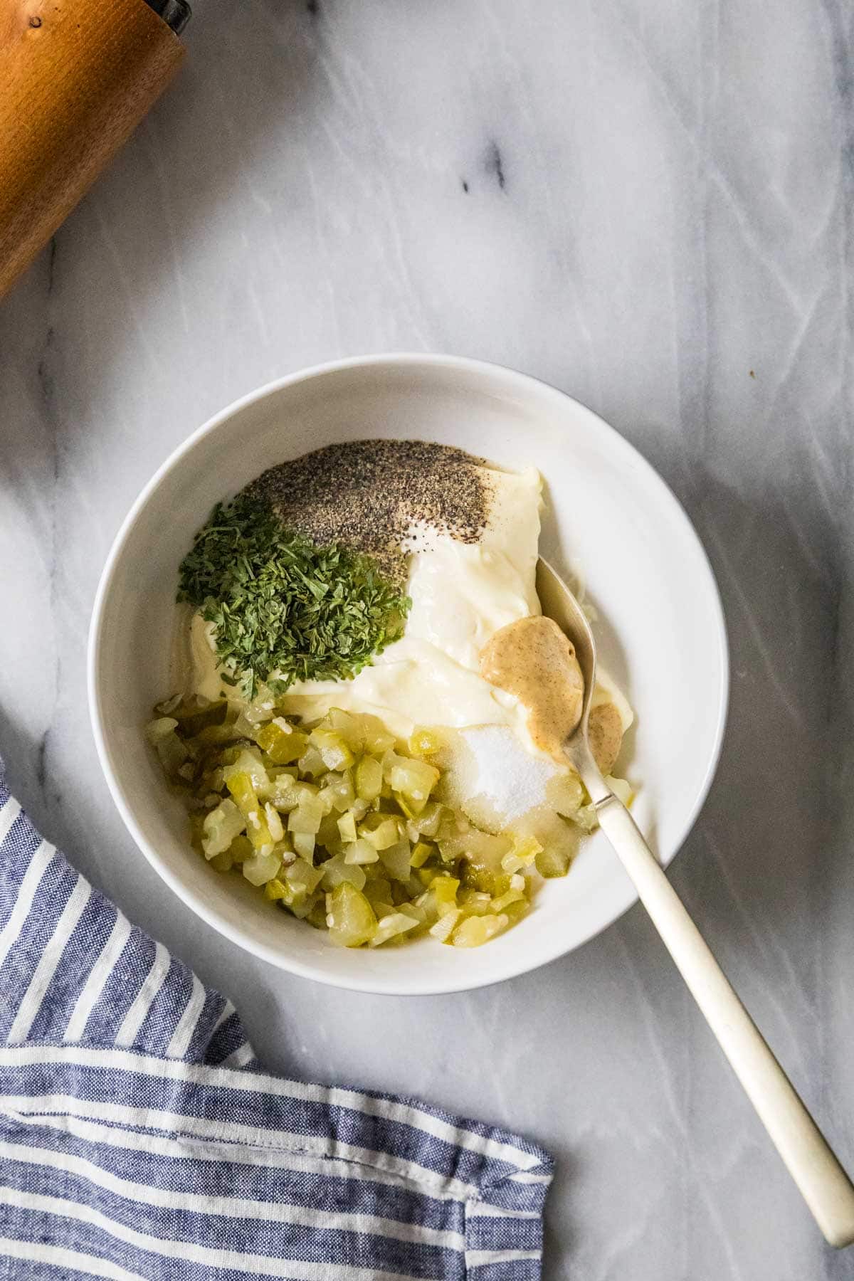 Overhead view of a bowl of mayo with chopped dill pickles, dijon, lemon juice, and more.