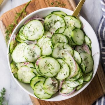 Overhead view of a serving bowl of cucumber salad made with dill and red onion.