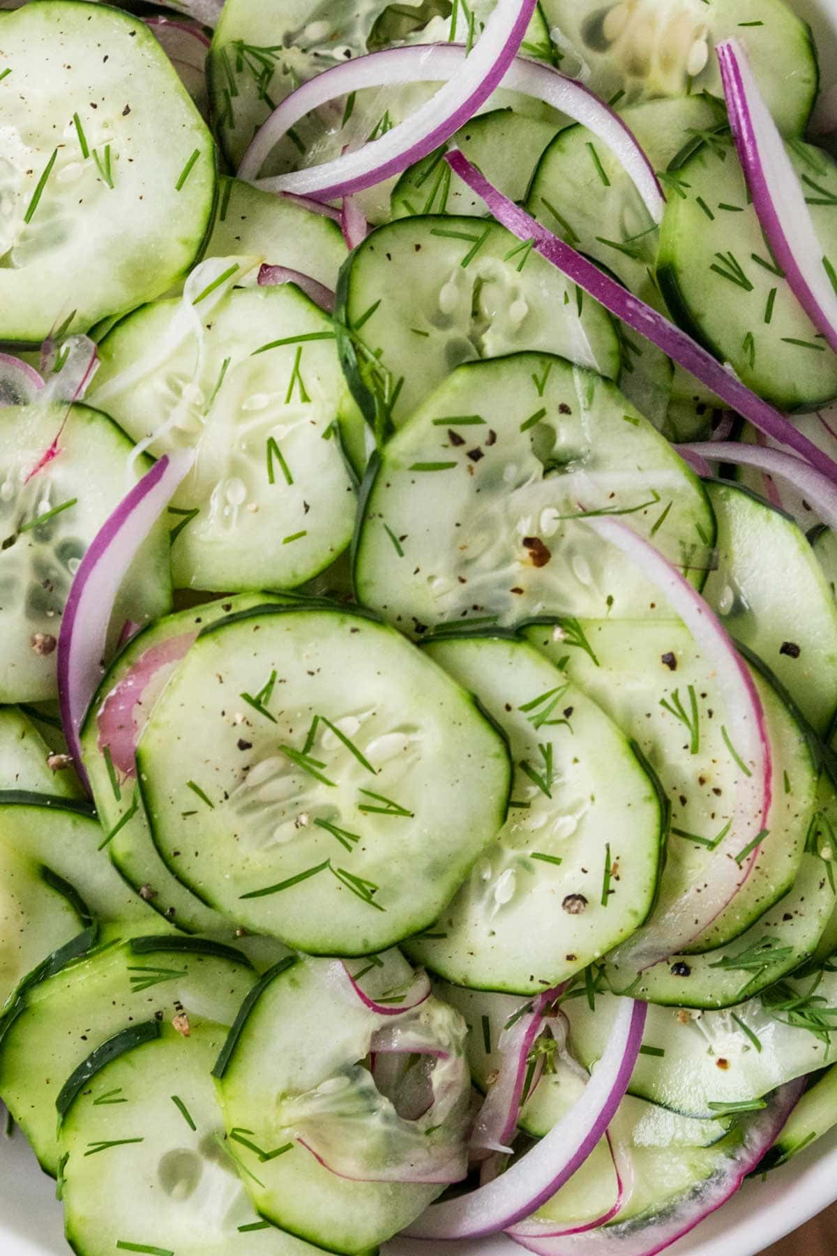 Close-up view of cucumber slices and red onion tossed in a dill dressing.