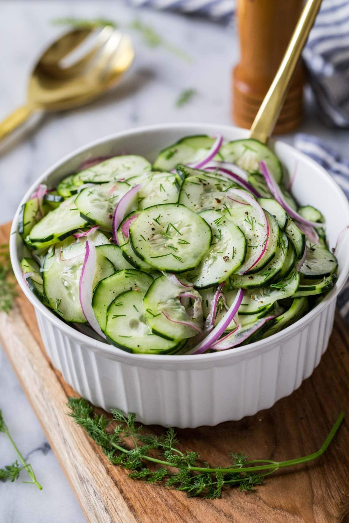 Salad made with cucumbers, red onion, and dill in a white serving bowl.