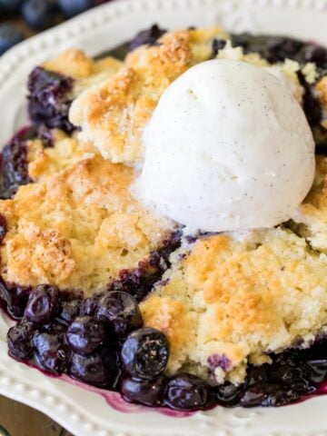 Serving of blueberry cobbler topped with a scoop of vanilla ice cream in a white dish.