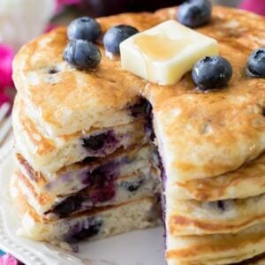 Stack of blueberry pancakes topped with blueberries, syrup, and a pat of butter.