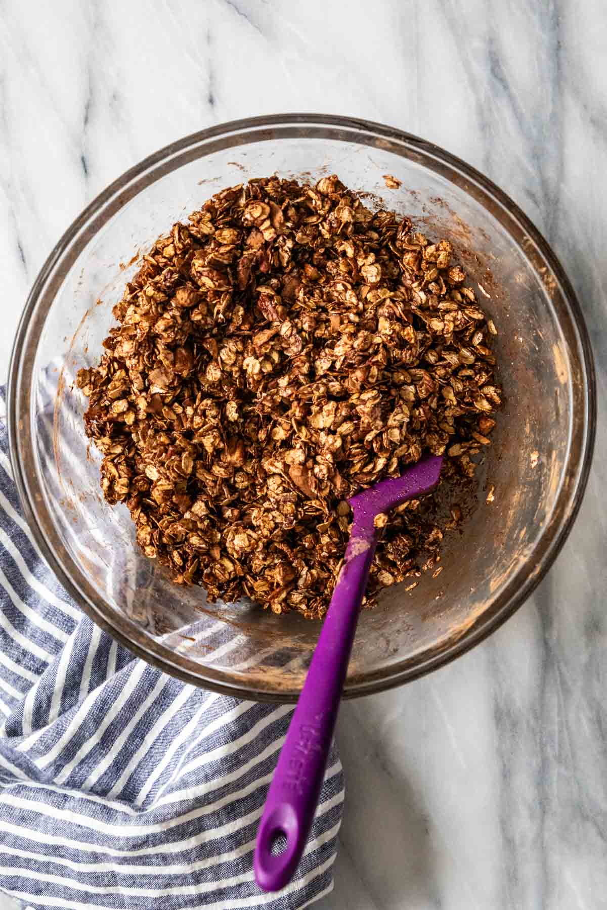 Overhead view of a bowl of oats, nuts, cocoa powder, and more combined with a spatula.