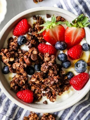Overhead view of chocolate granola sprinkled over a bowl of yogurt and berries.
