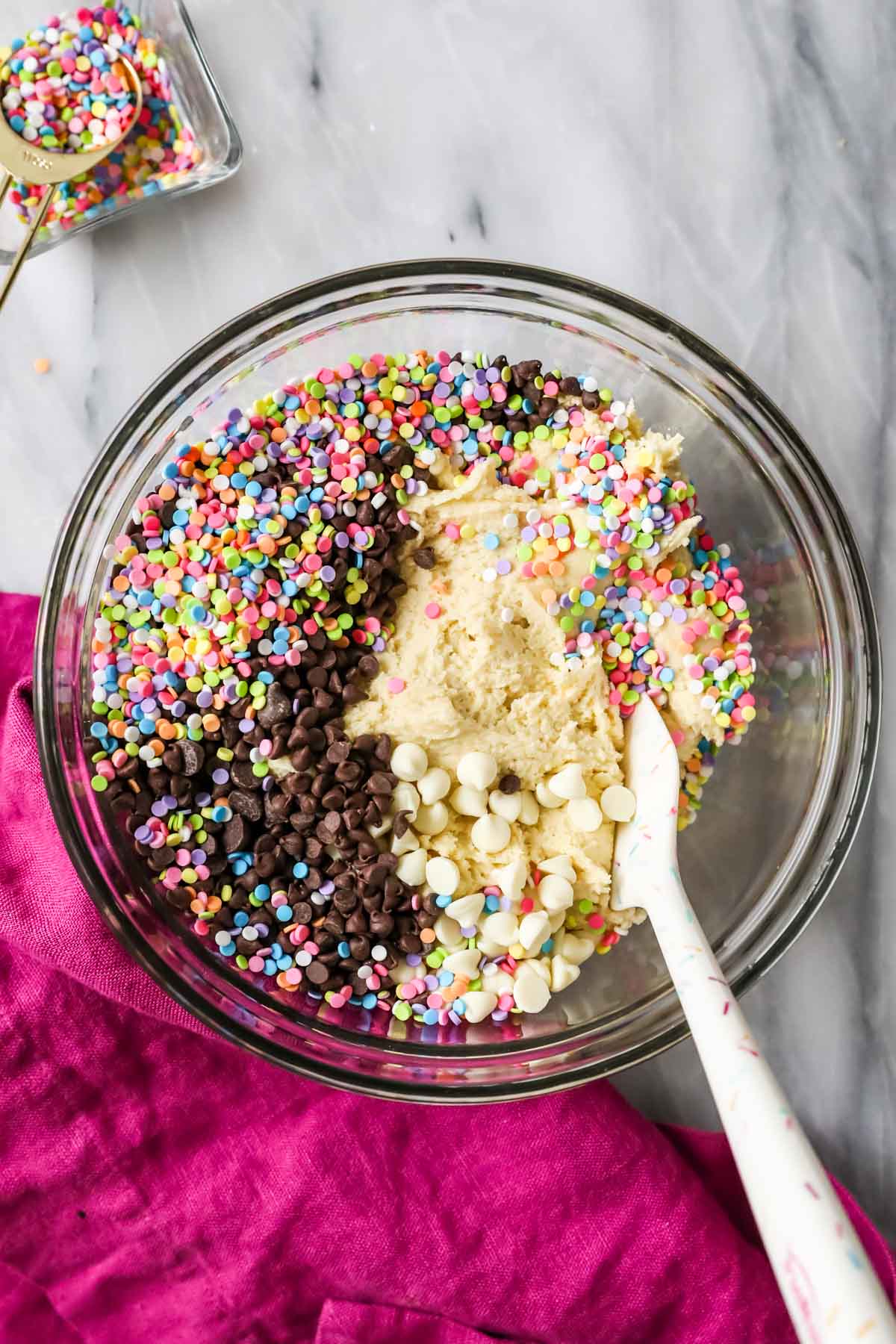 Overhead view of a bowl of cookie dough with several types of chocolate chips and sprinkles on top.