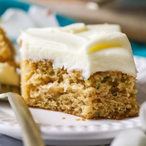 Square slice of zucchini cake topped with cream cheese frosting with one forkful sitting beside the slice.