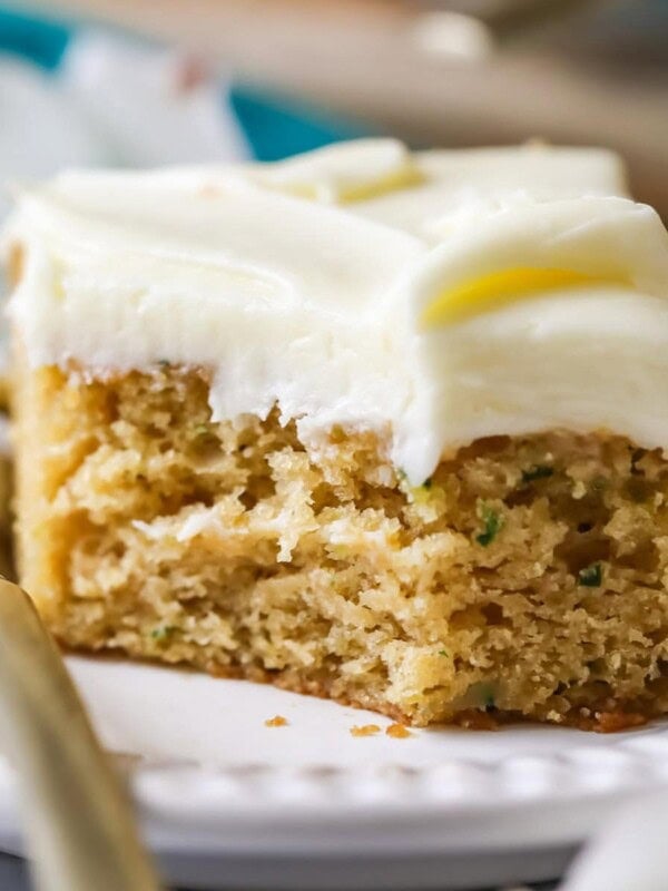 Square slice of zucchini cake topped with cream cheese frosting with one forkful sitting beside the slice.