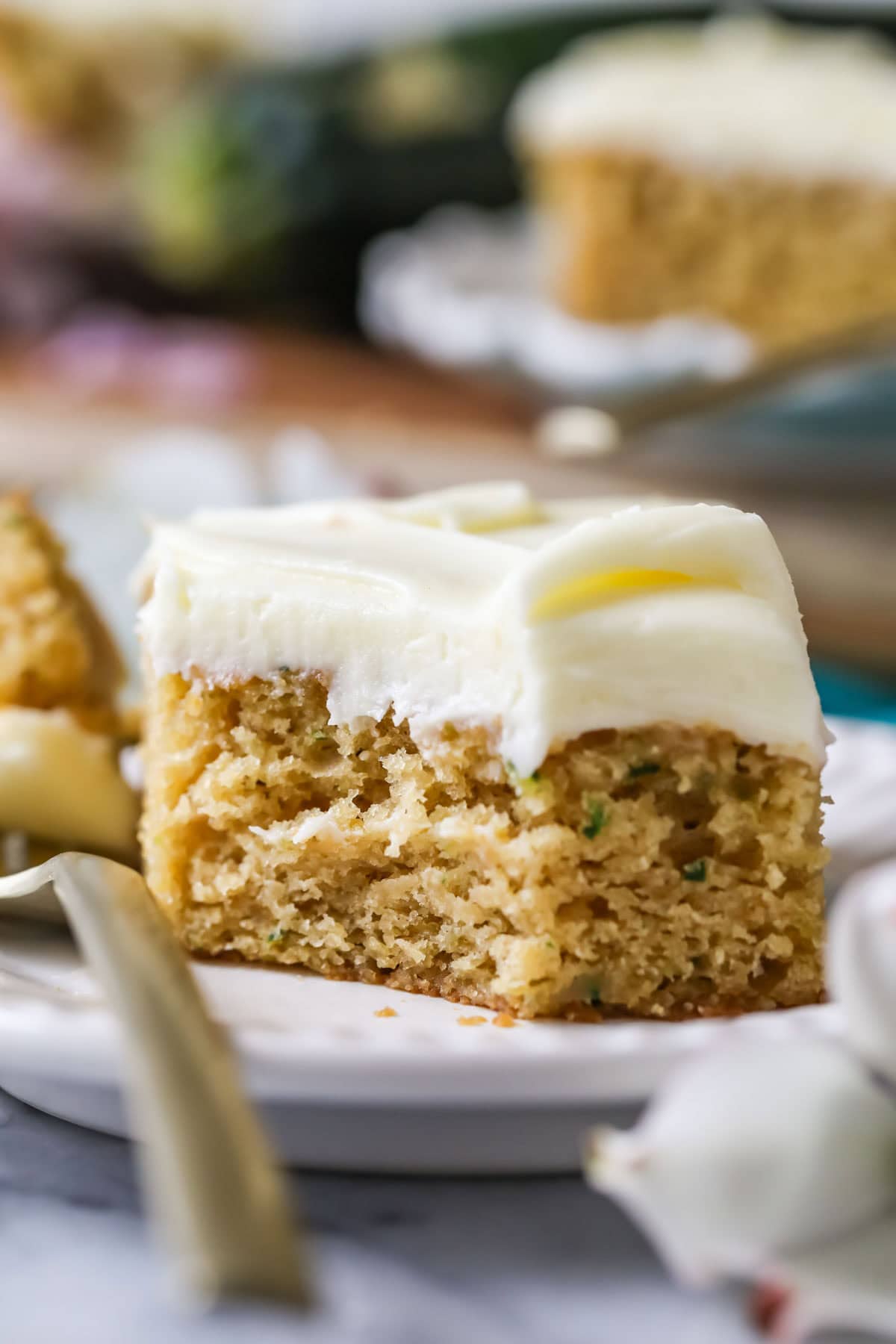 Square slice of zucchini cake topped with cream cheese frosting with one forkful sitting beside the slice.