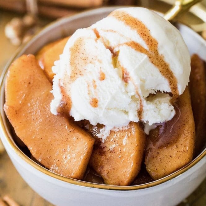 Serving of baked apples in a bowl with a scoop of vanilla ice cream on top.