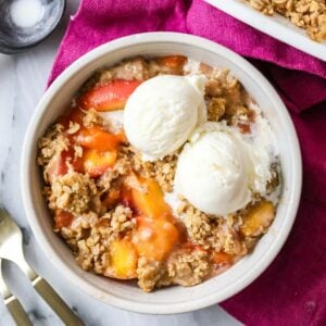 Overhead view of a bowl of peach crisp topped with vanilla ice cream.