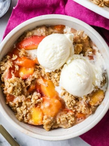 Overhead view of a bowl of peach crisp topped with vanilla ice cream.