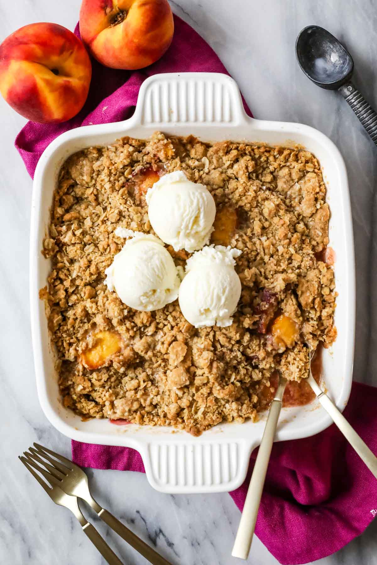 Overhead view of a peach dessert topped with an oat crumble and vanilla ice cream.