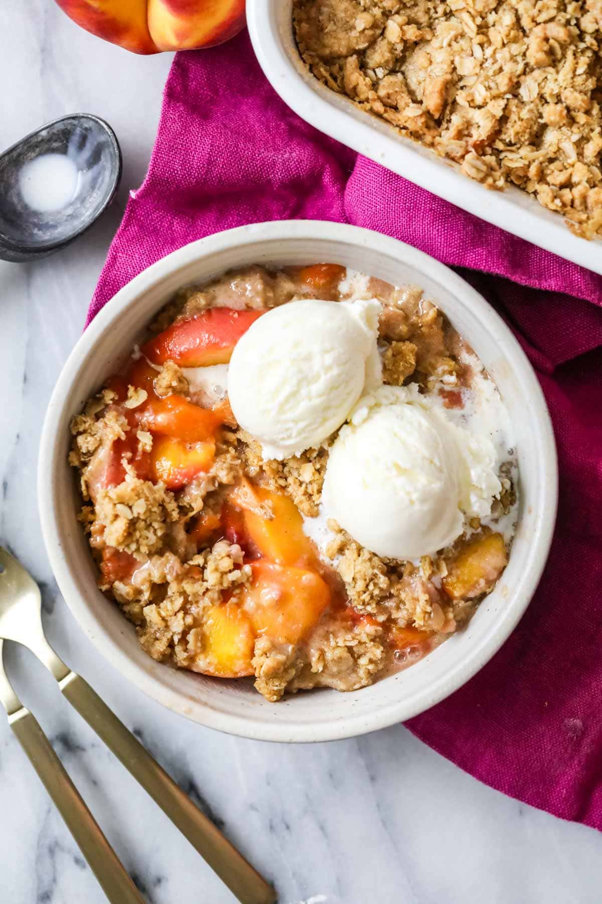 Overhead view of a bowl of peach crisp topped with vanilla ice cream.