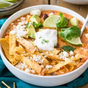 Overhead view of a bowl of chicken tortilla soup topped with tortilla strips, sour cream, lime, and cilantro.