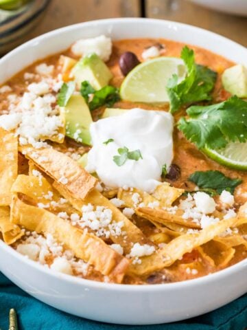 Overhead view of a bowl of chicken tortilla soup topped with tortilla strips, sour cream, lime, and cilantro.