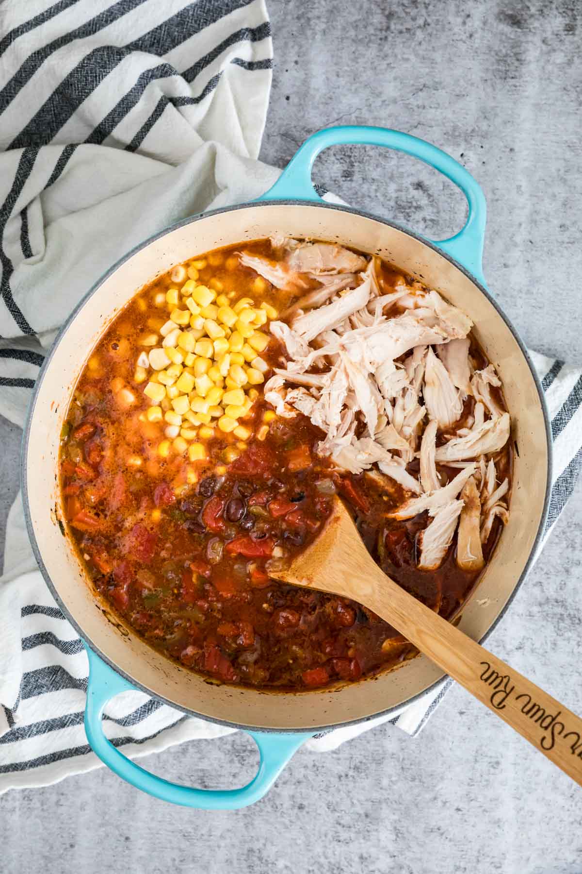 Overhead view of a pot of soup with shredded chicken, corn, and fire roasted tomatoes on top before stirring in.