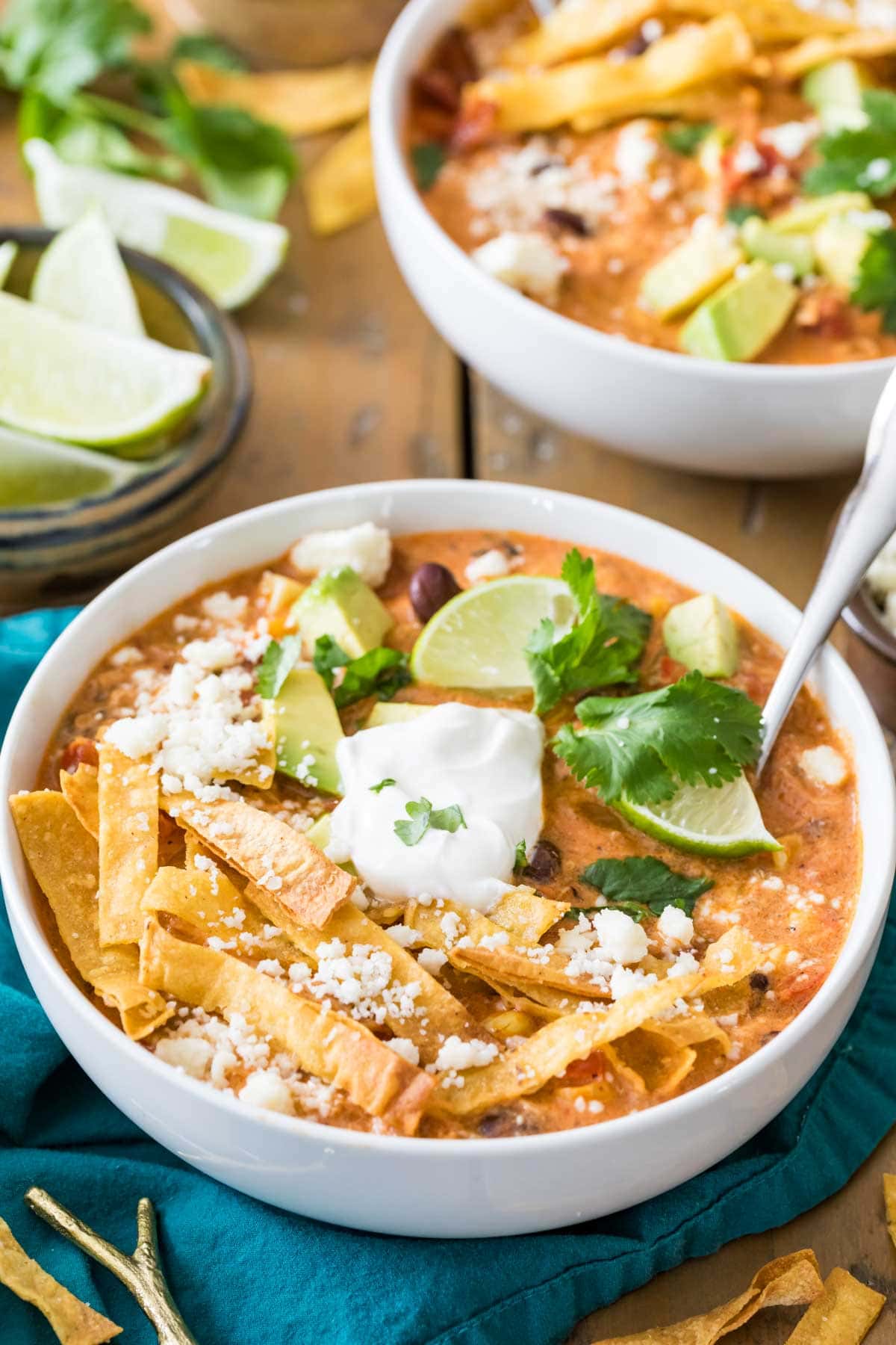 Overhead view of bowls of chicken tortilla soup topped with tortilla strips, sour cream, lime, and cilantro. 