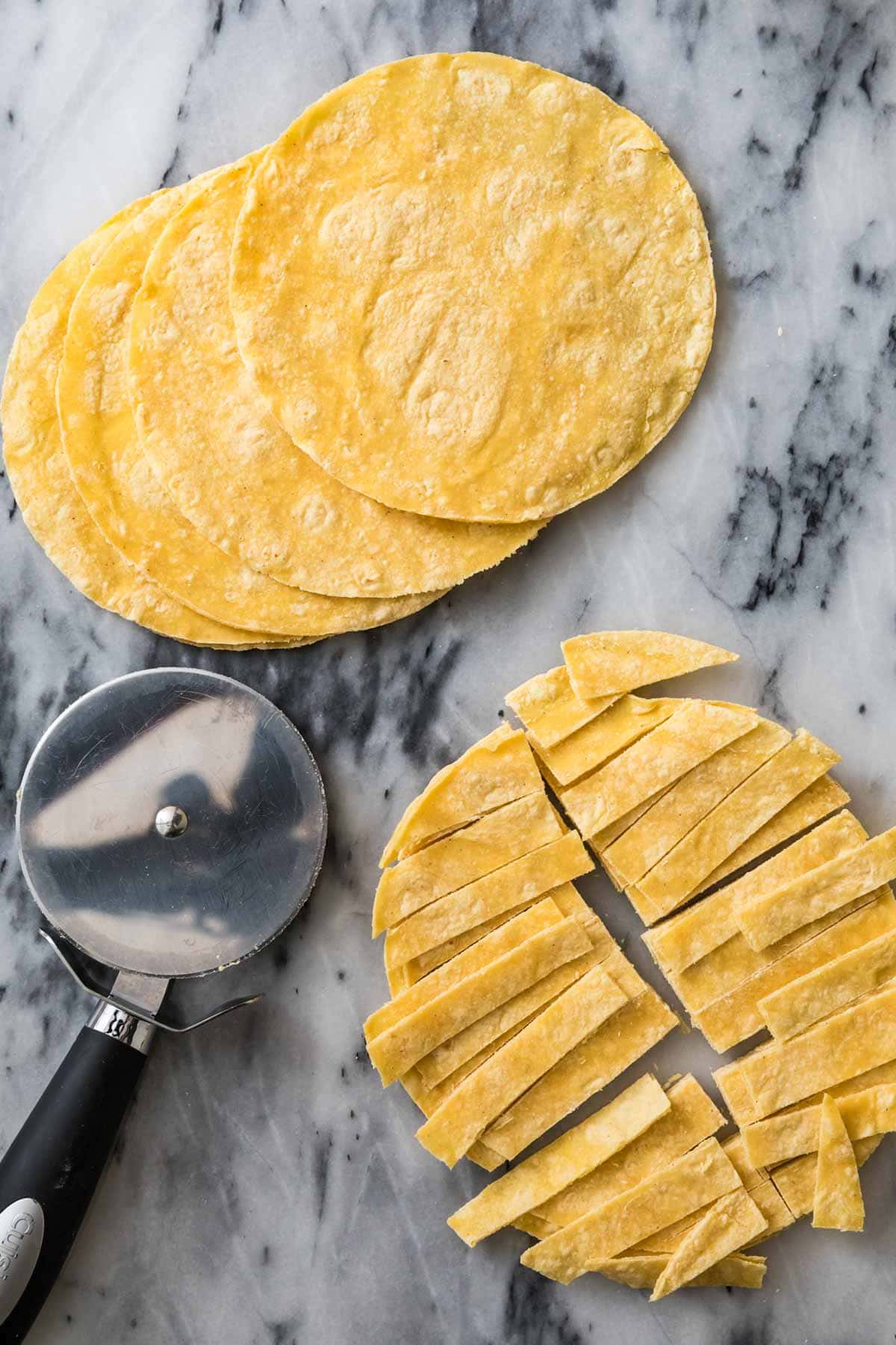 Corn tortillas being cut into strips with a pizza cutter.