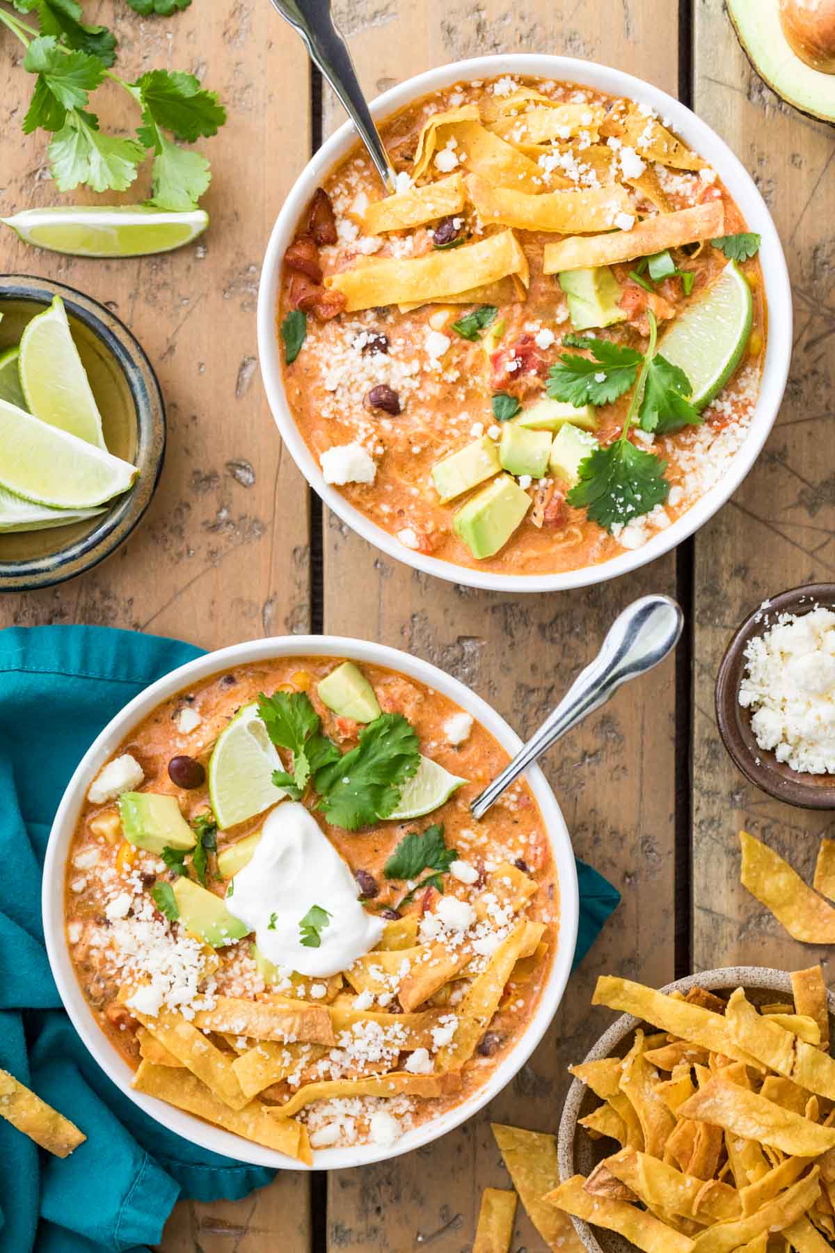 Overhead view of bowls of chicken tortilla soup topped with tortilla strips, sour cream, lime, and cilantro.