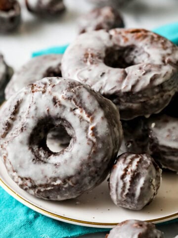 Old fashioned chocolate donuts with a vanilla glaze on a plate.