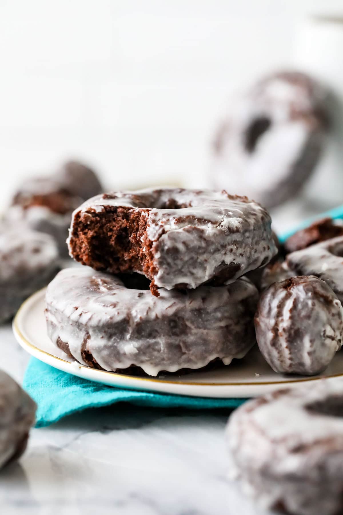 Bite missing from a glazed chocolate cake donut stacked on top of another donut on a plate.