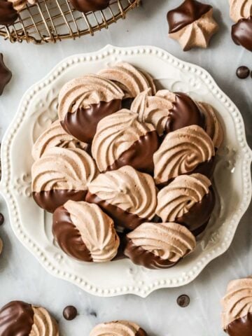 Overhead view of a plate of chocolate meringues that have been half dipped in chocolate.