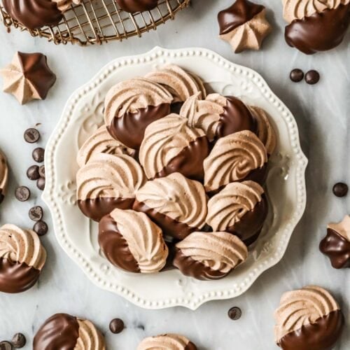 Overhead view of a plate of chocolate meringues that have been half dipped in chocolate.