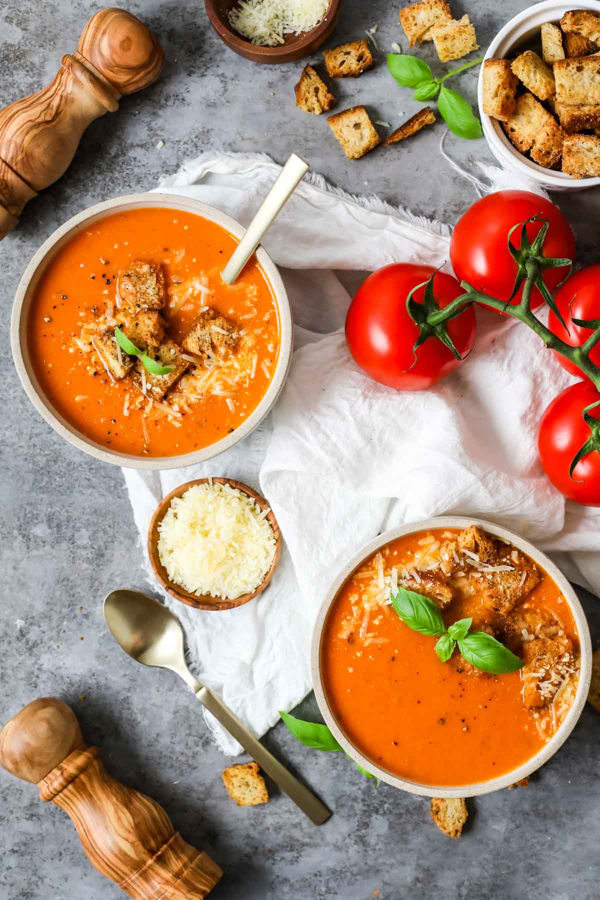 Overhead view of bowls of fresh tomato soup topped with basil, parmesan, and croutons.