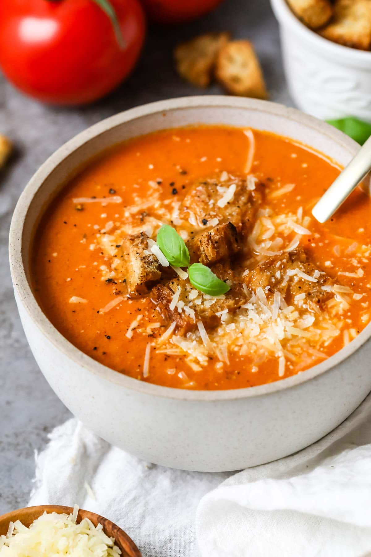 Close-up view of fresh tomato soup topped with basil, parmesan, and croutons.