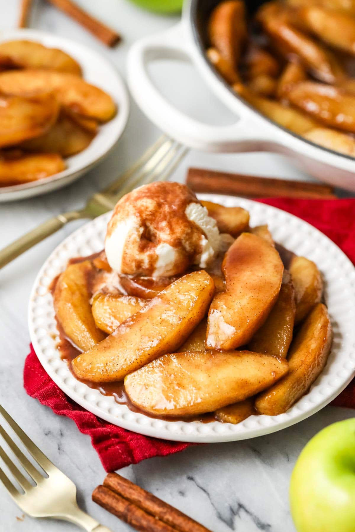 A scoop of vanilla ice cream on top of a plate of apples roasted with butter and spices.