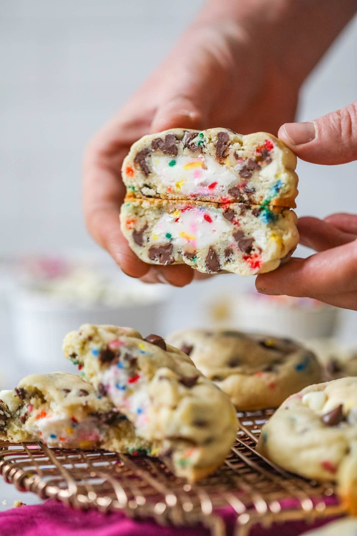 Hands holding a chocolate chip cookie that's been cut in half to show a frosting filled center.