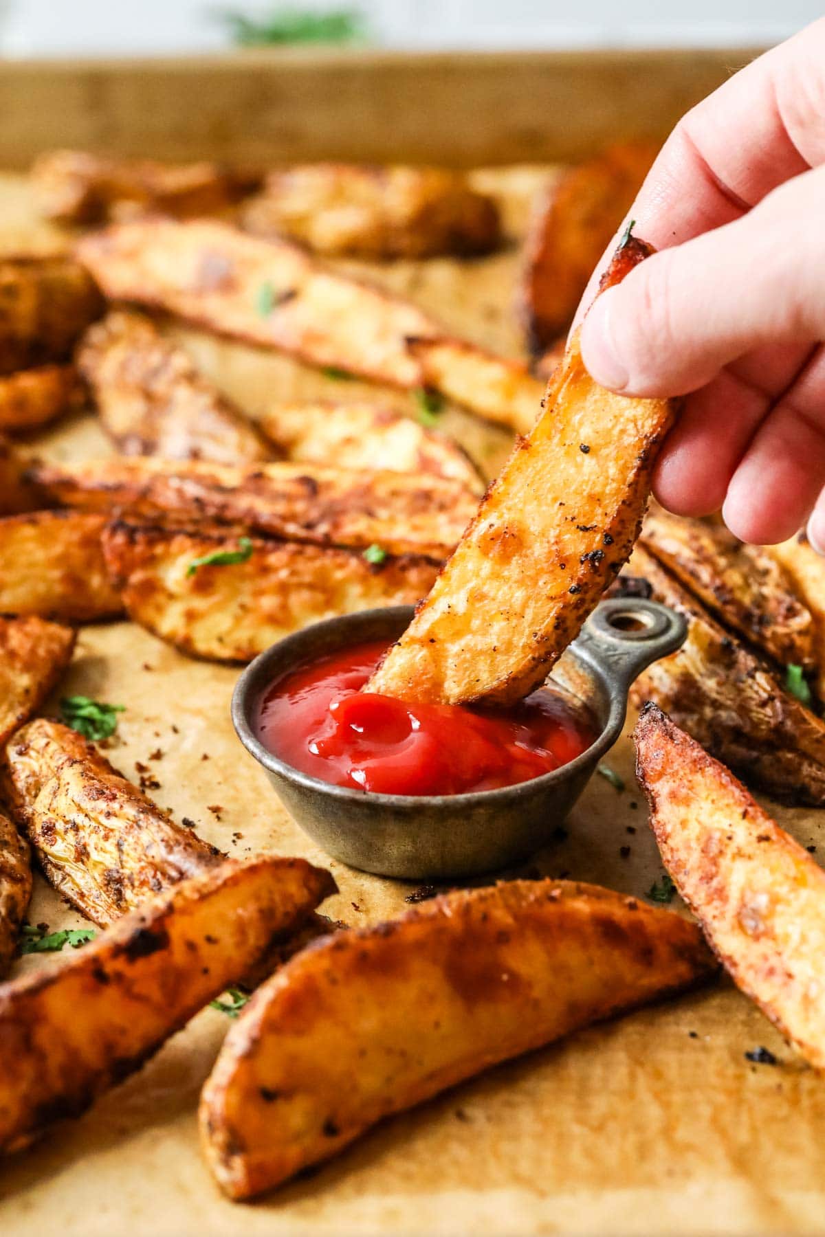 Tray of potato wedges with one wedge being dipped in ketchup in the center.