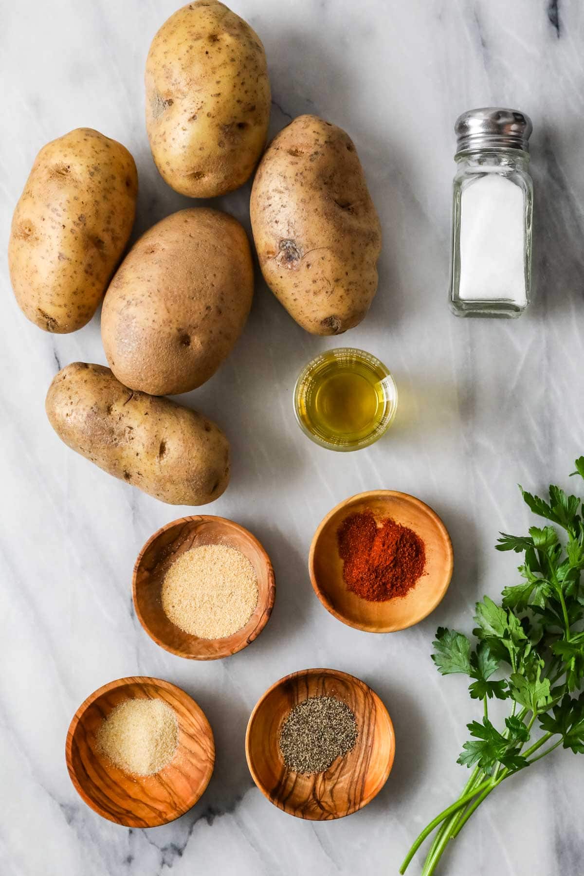 Overhead view of ingredients including potatoes, spices, oil, and salt.