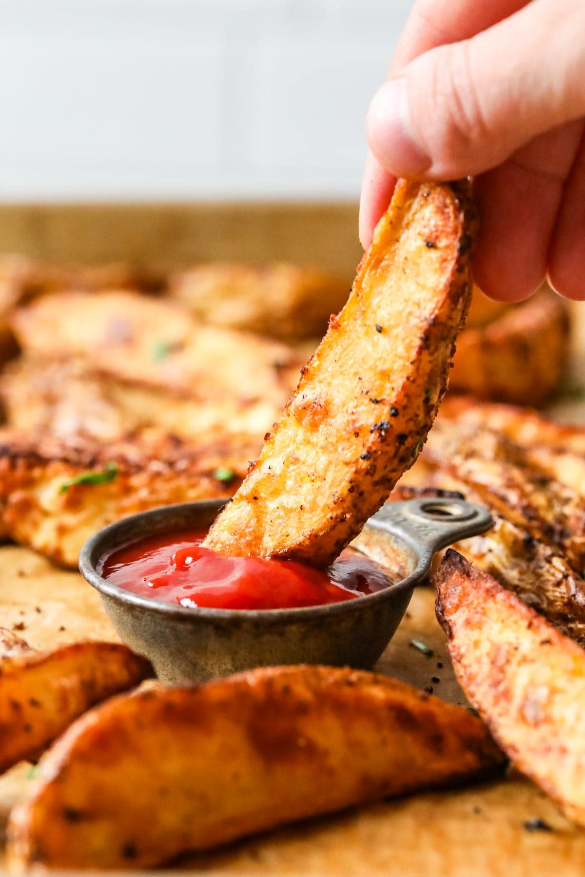 Close-up view of a potato wedge being dipped in ketchup.