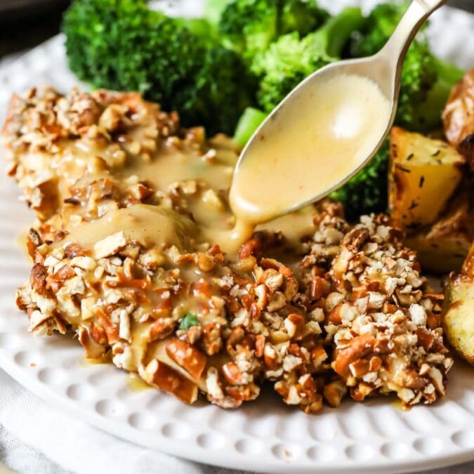 Honey mustard sauce being drizzled over pretzel crusted chicken.