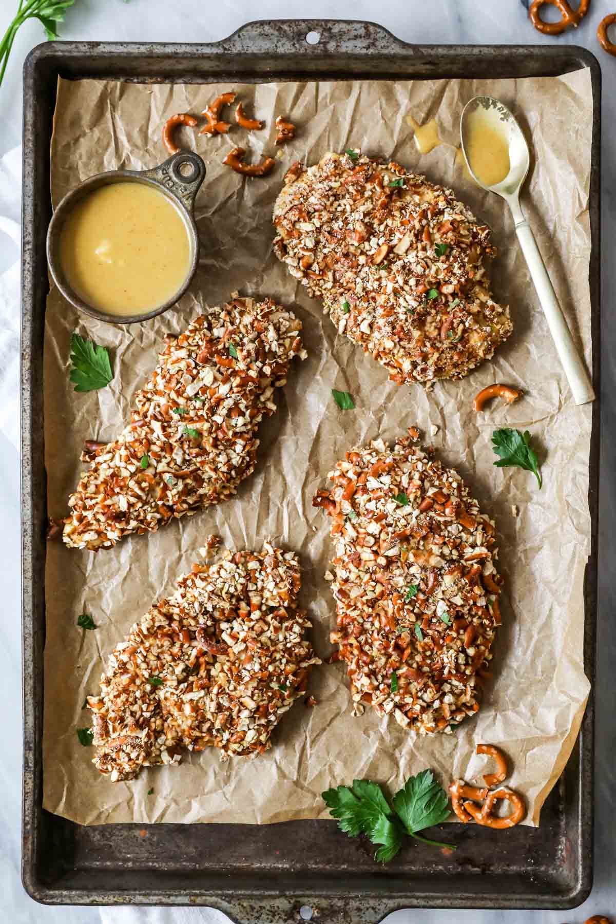 Overhead view of chicken breast cutlets encrusted with pretzels on a baking sheet.