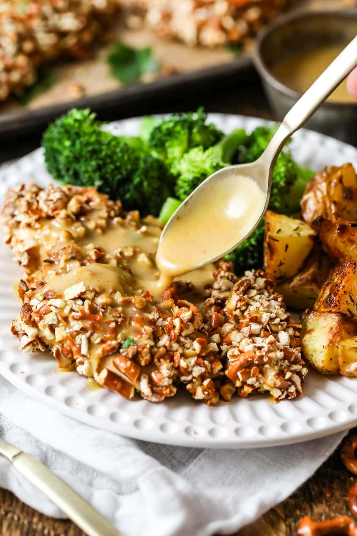 Honey mustard sauce being drizzled over pretzel crusted chicken.