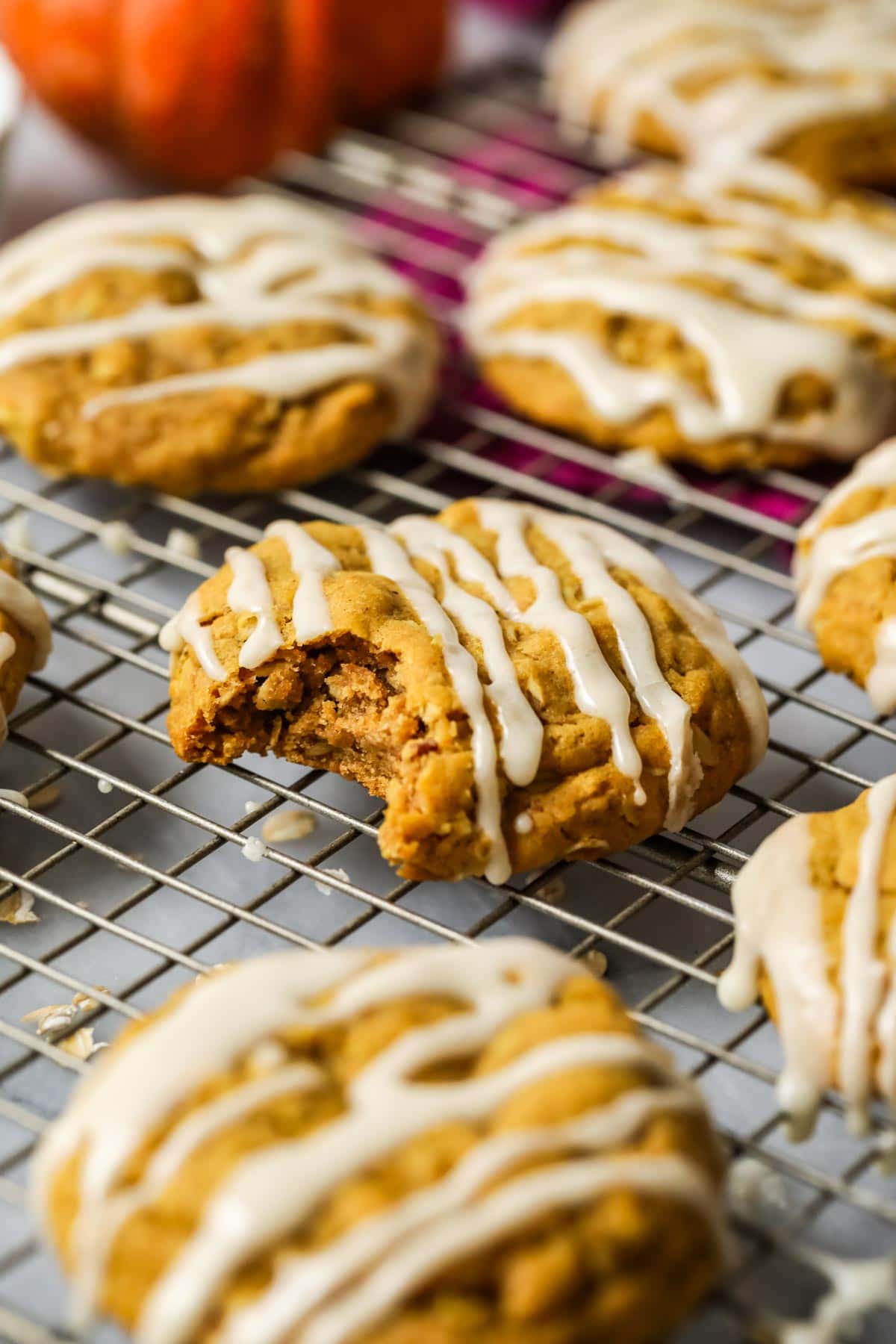 Close-up view of pumpkin oatmeal cookies topped with a glaze on a cooling rack.