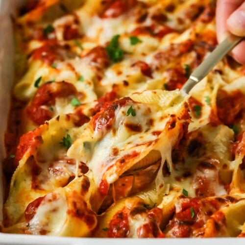 Spoon lifting a serving from a pan of stuffed shells.