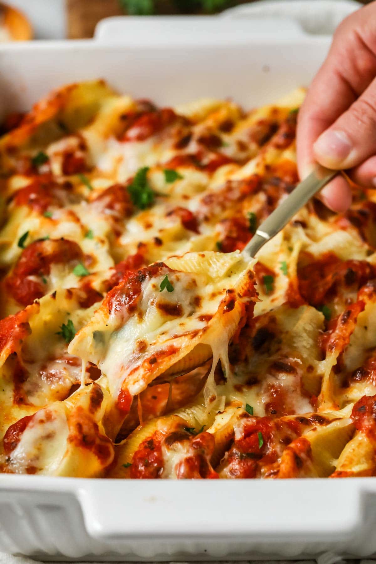 Spoon lifting a serving from a pan of stuffed shells.